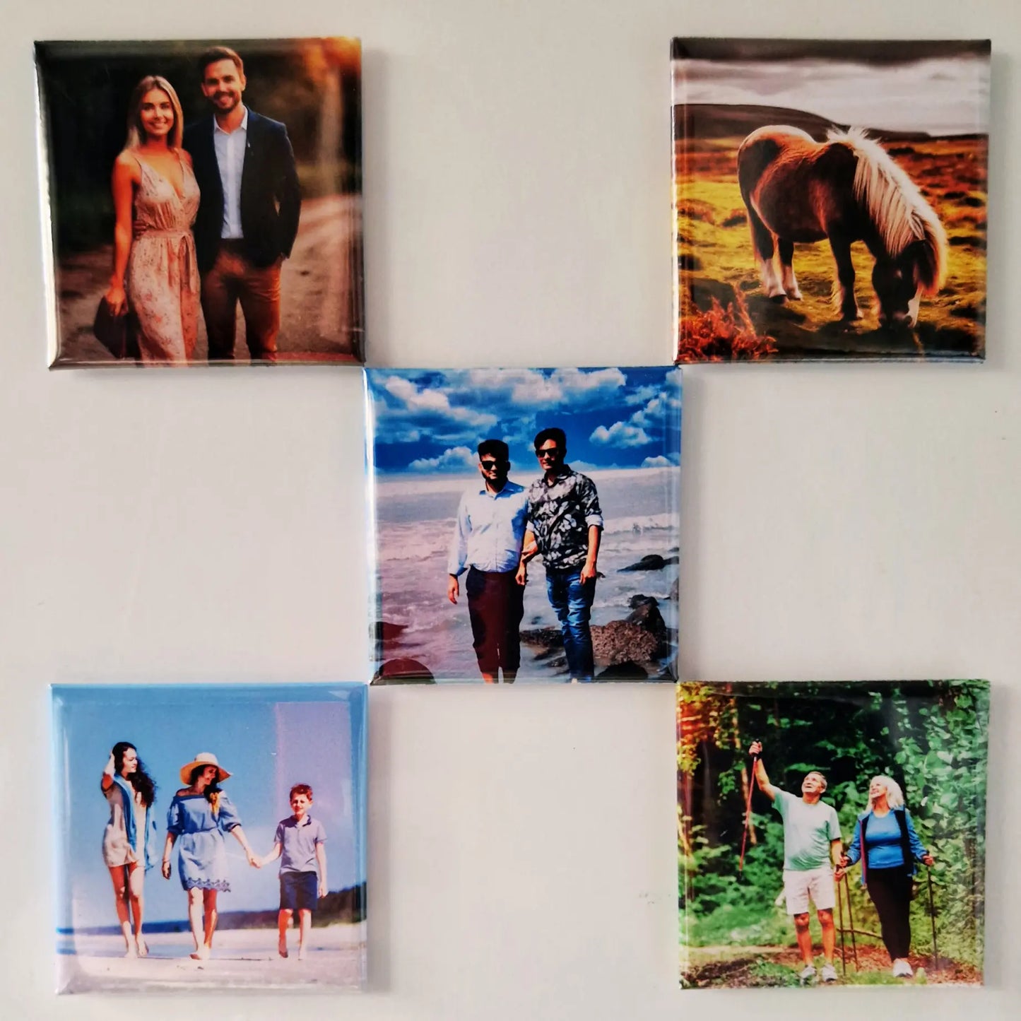 Five magnets arranged on a fridge in a grid layout, with four magnets forming a square and one placed in the center of the grid. Each magnet displays a different design, creating a balanced and organized look against the fridge's surface.