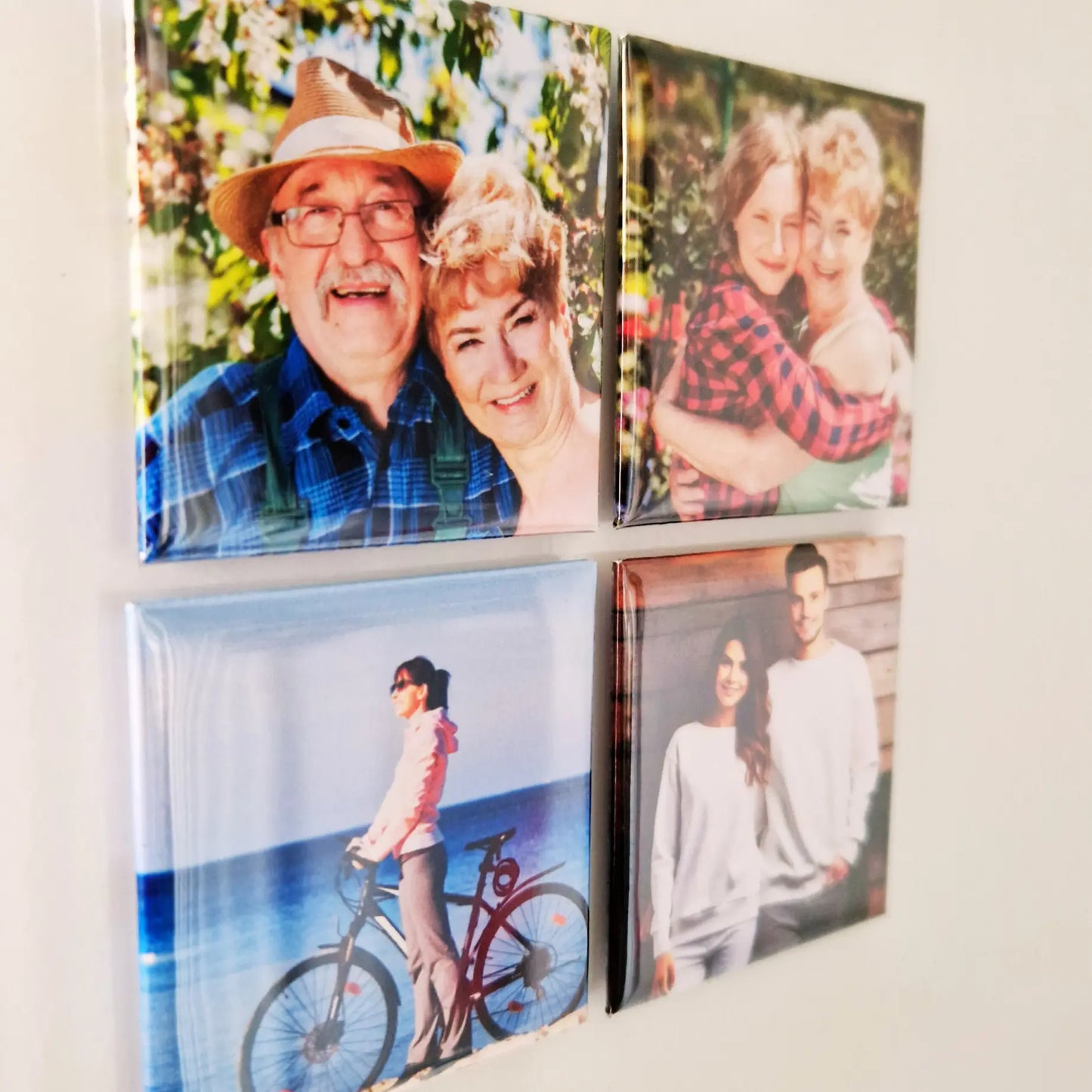 Four magnets arranged in a square layout on a fridge, viewed from an angled side perspective. The magnets are evenly spaced and feature different designs, with the fridge surface visible in the background, creating a clean, modern look.