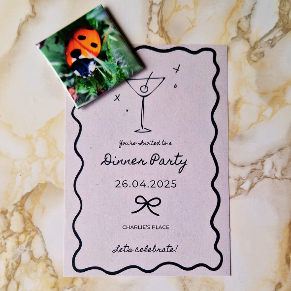 A single square magnet featuring a close-up image of a vibrant red and black ladybird on a green leaf. The magnet is holding a party invitation against a marbled background.