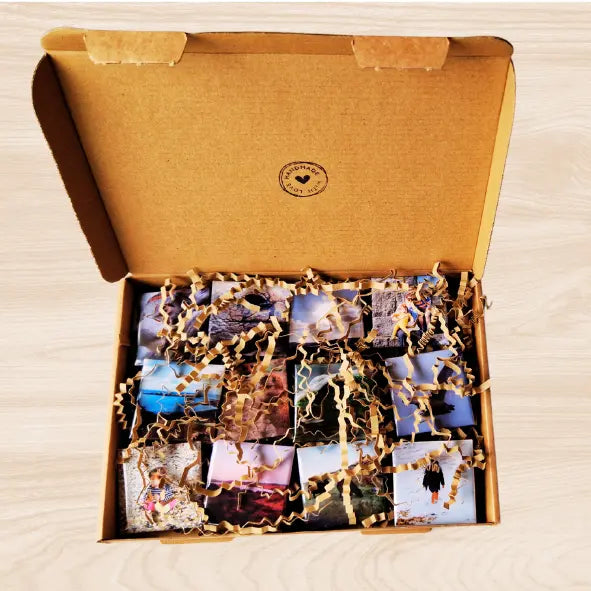 A set of 12 custom fridge magnets neatly arranged inside a cardboard shipping box. The magnets rest on a layer of protective corrugated paper. The box lid features a black ink stamped design that reads "Handmade with Love." The magnets are glossy and vibrant, showcasing a variety of images. The packaging emphasizes a handmade and carefully crafted product, ready for gifting or personal use.
