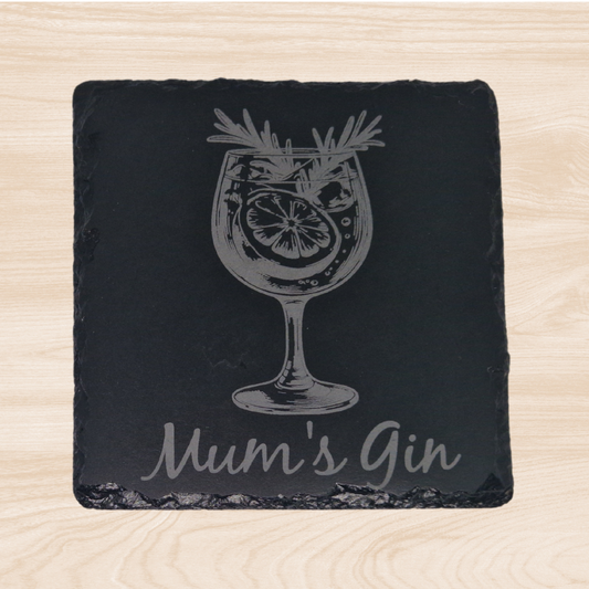 A smooth black slate coaster with an engraved design of a gin glass filled with ice and garnishes. Below the glass, the words "Mum's Gin" are elegantly engraved, creating a stylish and personalized touch. The natural texture of the slate contrasts with the crisp engraving