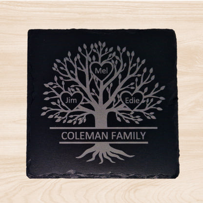 An engraved slate coaster featuring a family tree design. The design includes a detailed tree illustration with three hearts, each containing a family member's name. The family surname is engraved in capital letters across the bottom, integrated through the tree trunk, symbolizing strength and connection.