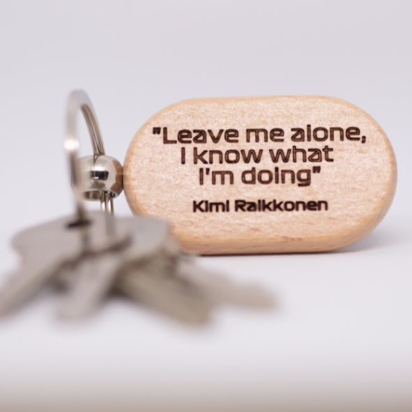 A wooden keychain engraved with the quote "Leave me alone, I know what I'm doing," attributed to Kimi Räikkönen. The text is bold and clear, with a simple, clean design.