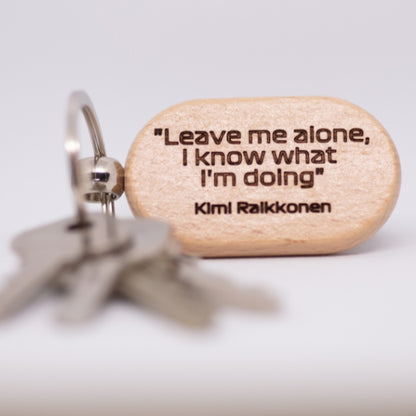 A wooden keychain engraved with the quote "Leave me alone, I know what I'm doing," attributed to Kimi Räikkönen. The text is bold and clear, with a simple, clean design.