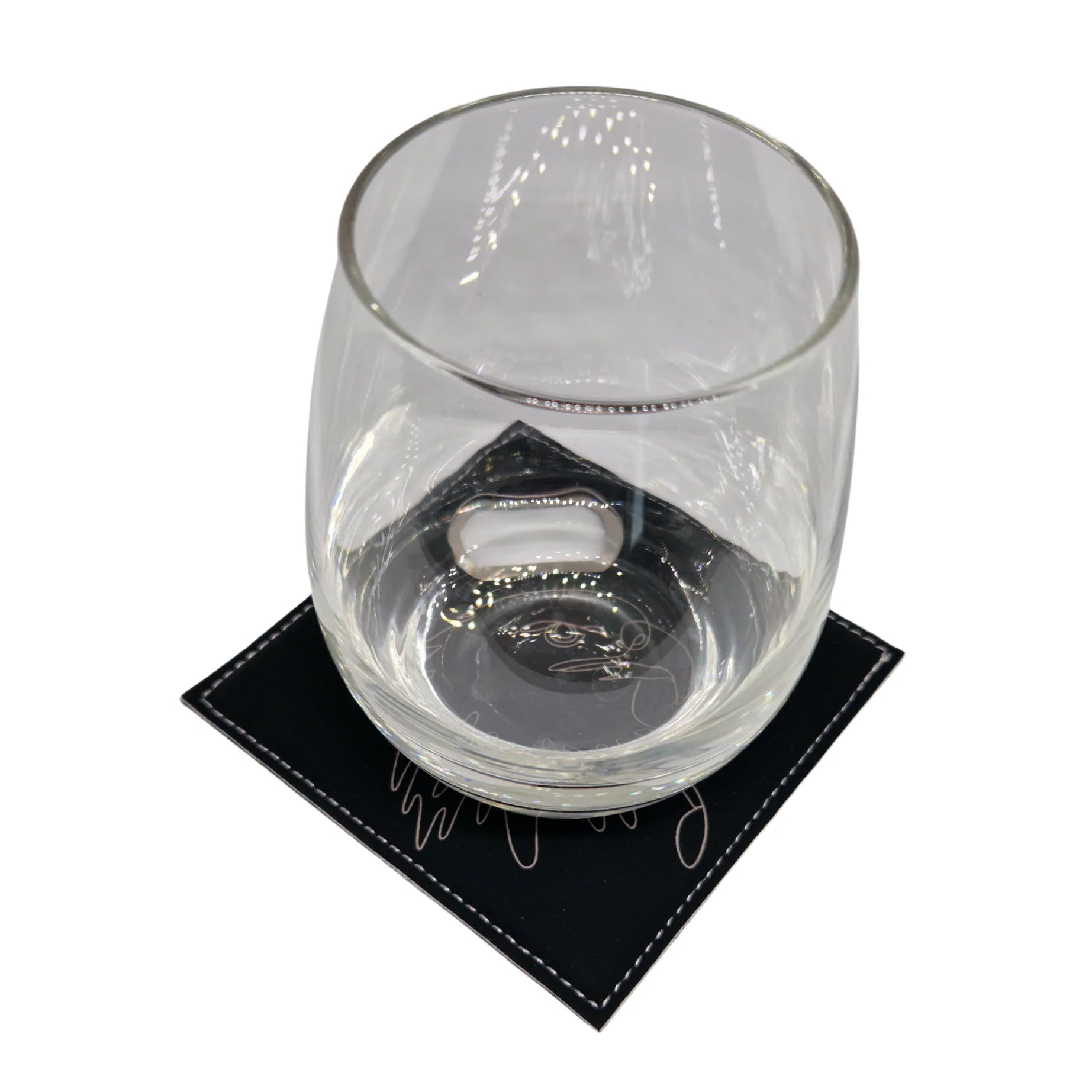 Short glass placed on a black leather coaster with intricate line art design.