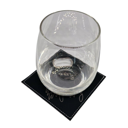 Short glass placed on a black leather coaster with intricate line art design.