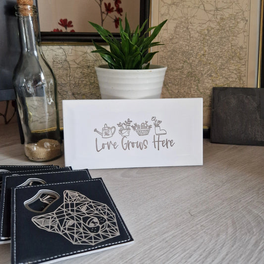 Engraved ceramic garden tile with 'Love Grows Here' on a desk, showcasing its elegant design.