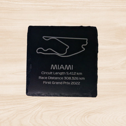 A black slate coaster featuring an engraved design of the Miami racetrack. The engraving includes detailed outlines of the circuit, along with text listing the circuit length, race distance, and the year the track held its first Grand Prix. The sleek, engraved lines contrast with the natural rough texture of the slate, creating a unique, informative design.