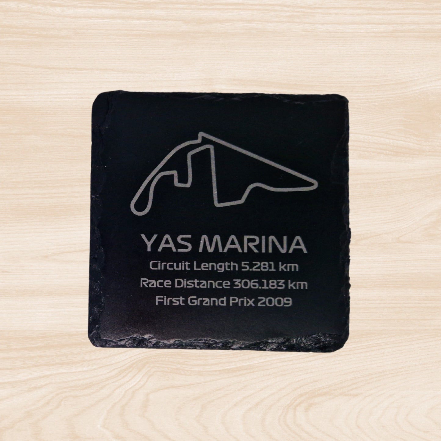 A black slate coaster featuring an engraved design of the Zandvoort racetrack. The engraving includes detailed outlines of the circuit, along with text listing the circuit length, race distance, and the year the track held its first Grand Prix. The sleek, engraved lines contrast with the natural rough texture of the slate, creating a unique, informative design.